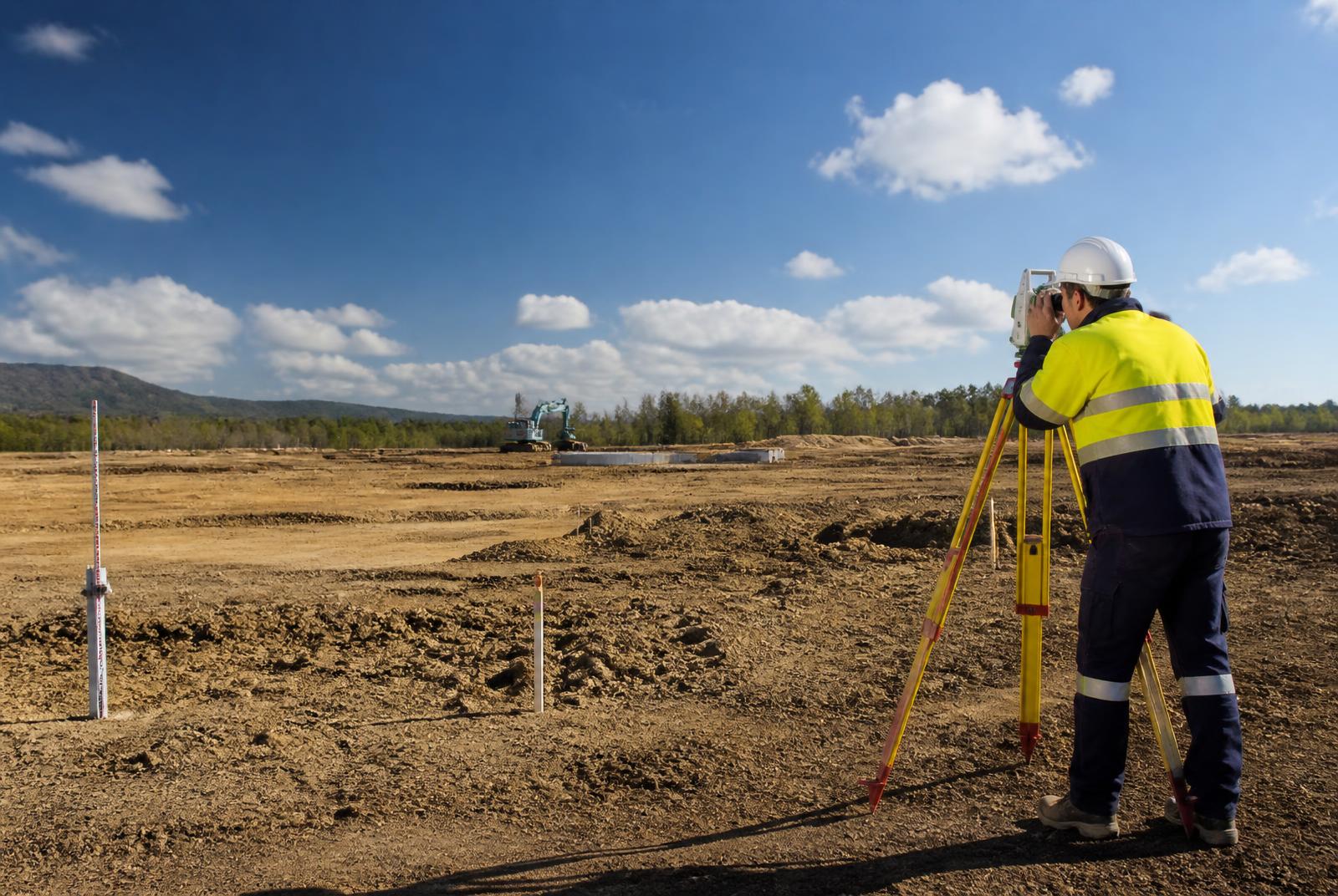 Survey engineer using a total station and monitoring markers to assess settlement across an earthworks site